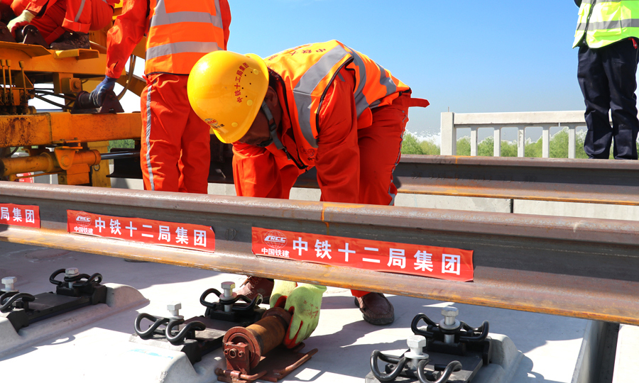 建设者在行进的机车上安装了物理临近报警系统，当携带有电子施工防护牌的现场施工作业人员进入设置的危险距离时，该系统会语音报警提示机车司机，并对现场施工防护员发出声光报警提示。同时，项目部调度中心技术人员还在机车上安装嵌入了国内自主研发的“北斗”定位车载定位系统，两项技术的“联姻”能够保证铺轨作业时精准定位机车行进位置，并采取在机车前后方安装摄像头的方式，实时传输线路上机车运行画面和行驶速度，确保铺轨作业运输智能化、信息化。图为安装长轨导向轮。