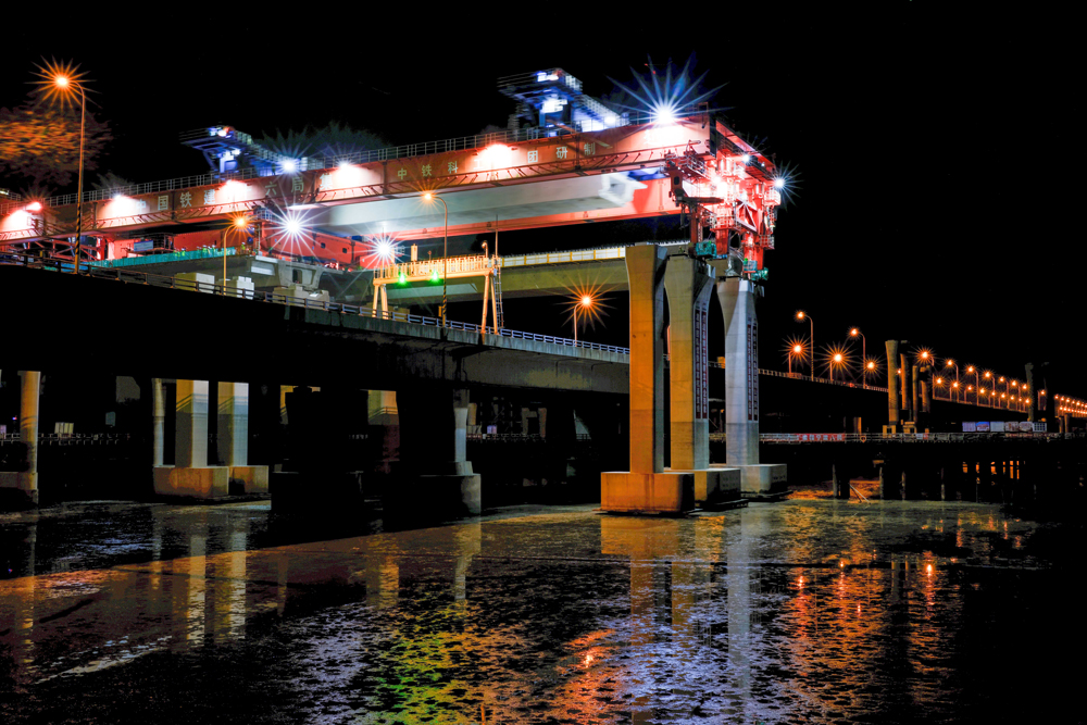 项目团队围绕海上50米大跨径、1800吨超大吨位整孔预制箱梁运输两个方面开展科研攻关，研制了我国自主研发、目前世界上最大的公路架桥机“越海号”开展“梁上运架”施工，成功攻克箱梁单体重量大、超高桥面渐变横坡、高低墩及1800米超小曲线半径等技术难题，确保了箱梁架设和金塘大桥运营安全，创下了国内采用“梁上运架”技术单体最重的整孔预制箱梁施工纪录。图为跨金塘大桥架梁施工现场。