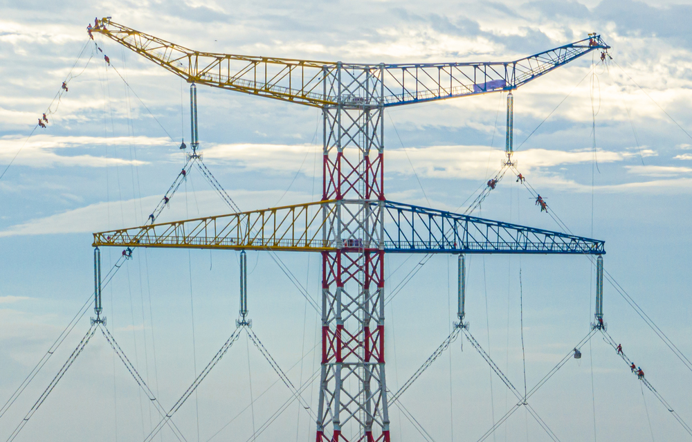 图为狮南甲乙线狮子洋大跨越新铁塔，塔高264.5米刷新国内水上输电铁塔新纪录，施工人员在进行线路附件安装，该工程改造后可提升线路输电容量40%。