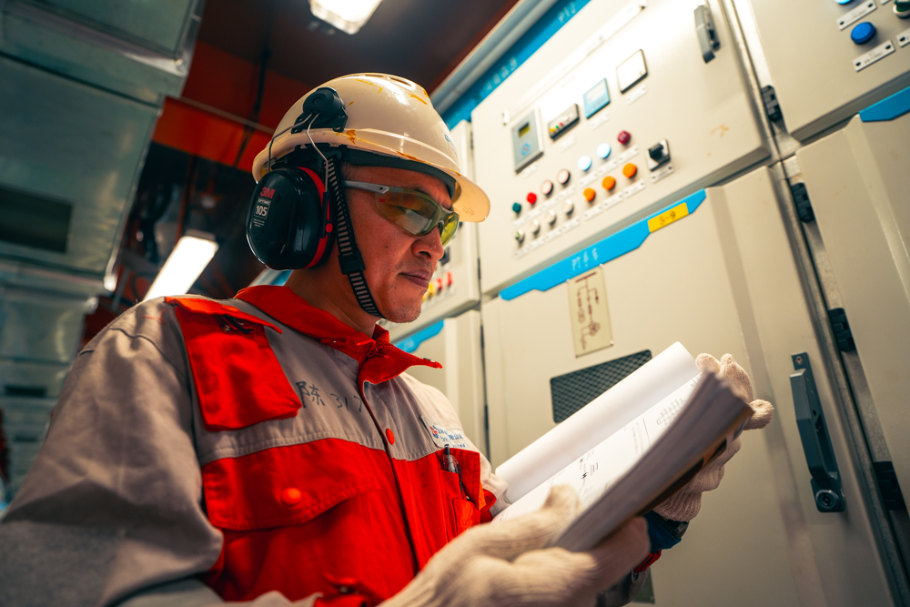 曹妃甸作业公司建立油井经济效益模型，按照效益分类管理油井，同时加强多专业联动，开展增储挖潜工作，立足平台内“挖”外“扩”，实现所有油田主力平台加挂井槽，三年内新增槽口90余个，开发新井超140口。图为海上平台电气工程师对照图纸进行故障排查工作。